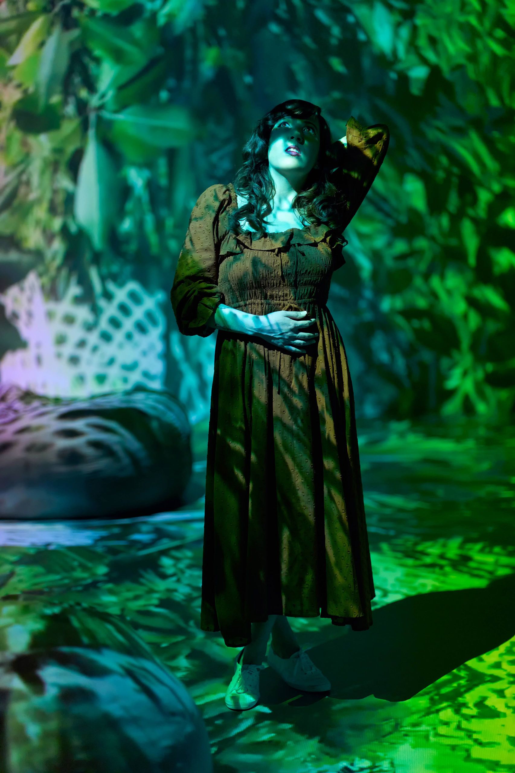 Artistic portrait of a woman in an olive dress illuminated with projected green botanical lighting