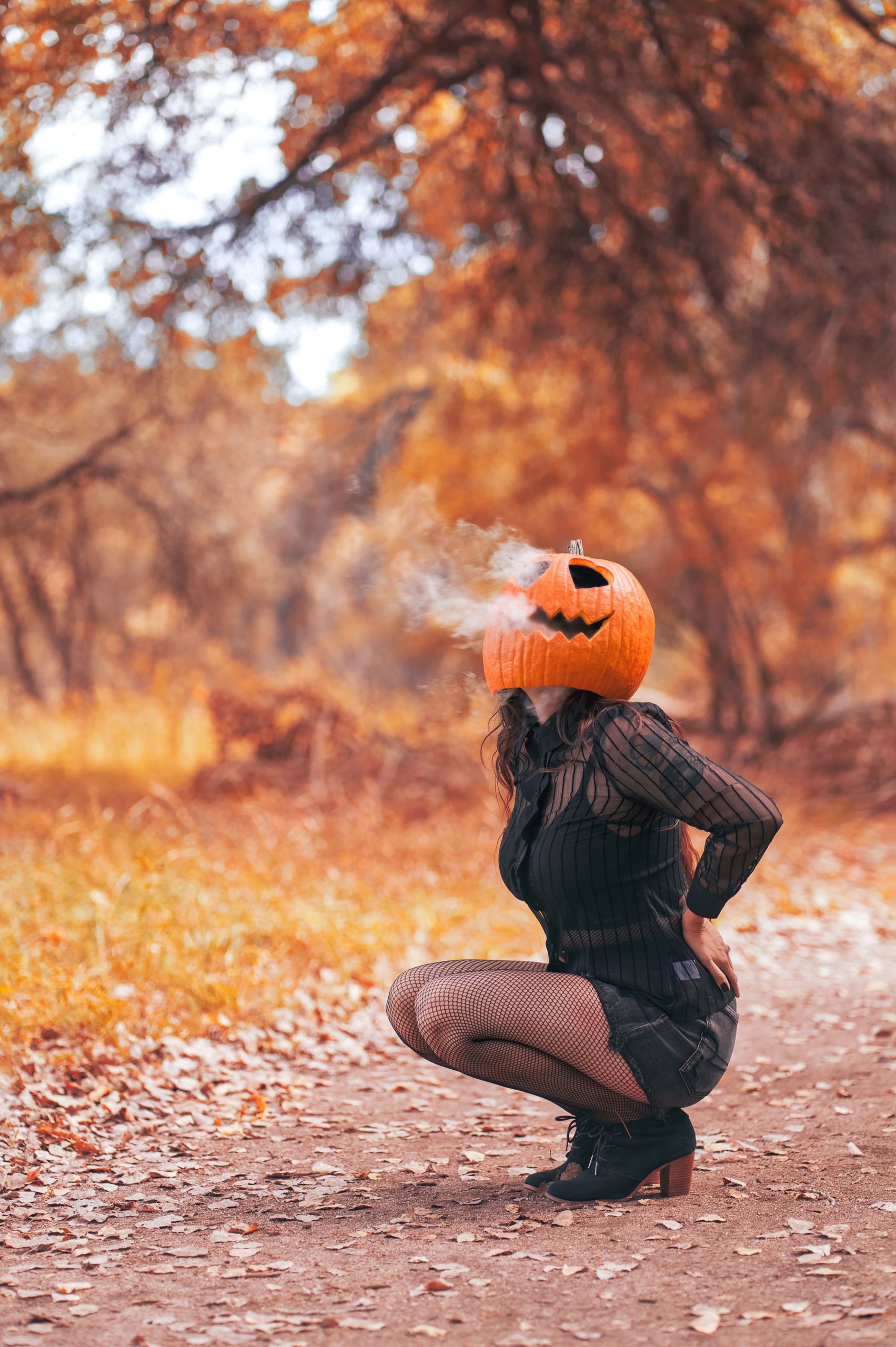 Person in autumn woods wearing a carved jack-o'-lantern on their head with smoke billowing out